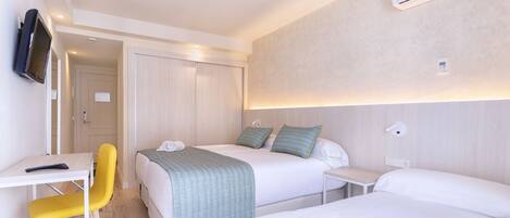 A hotel room with two beds, a desk with a chair, a TV, and an air conditioner.