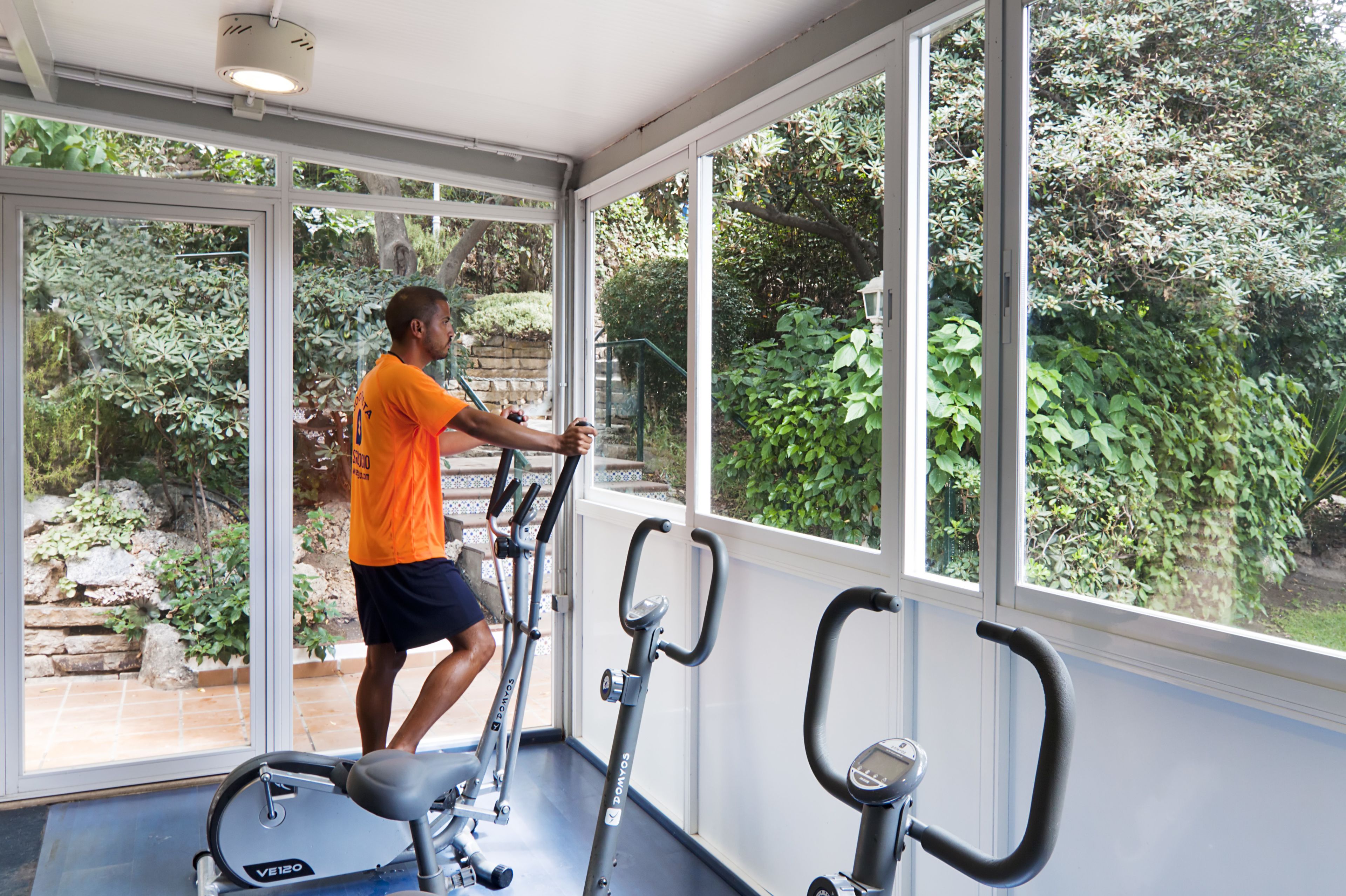 Une salle de sport équipée de matériel d’exercice et dotée de grandes fenêtres donnant sur un espace verdoyant.