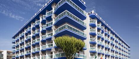 Un hotel de varios pisos con balcones, una entrada principal y un estacionamiento.