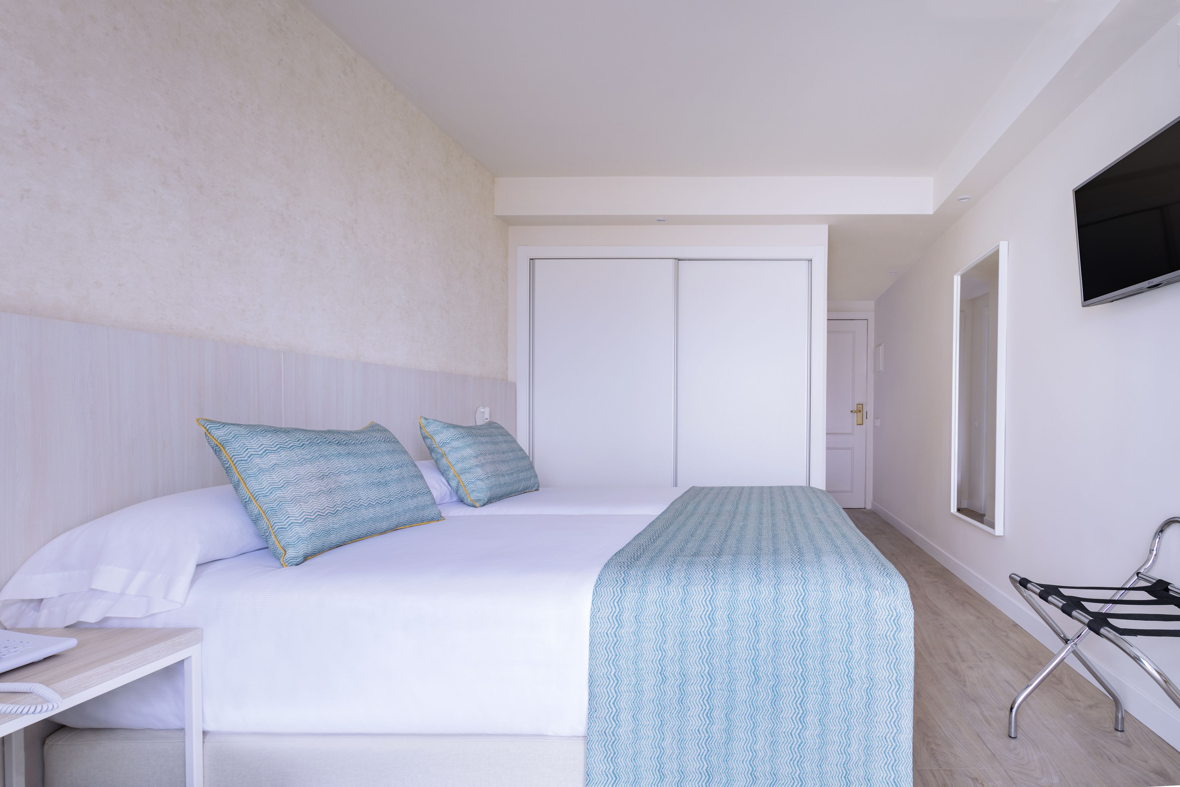 A hotel room with a bed, a desk, a chair, a TV, and a door.