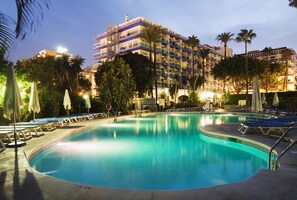 A hotel pool area with lounge chairs and umbrellas, surrounded by palm trees and a multi-story building with balconies. - Hotel Palmasol Puerto Marina (Benalmádena)