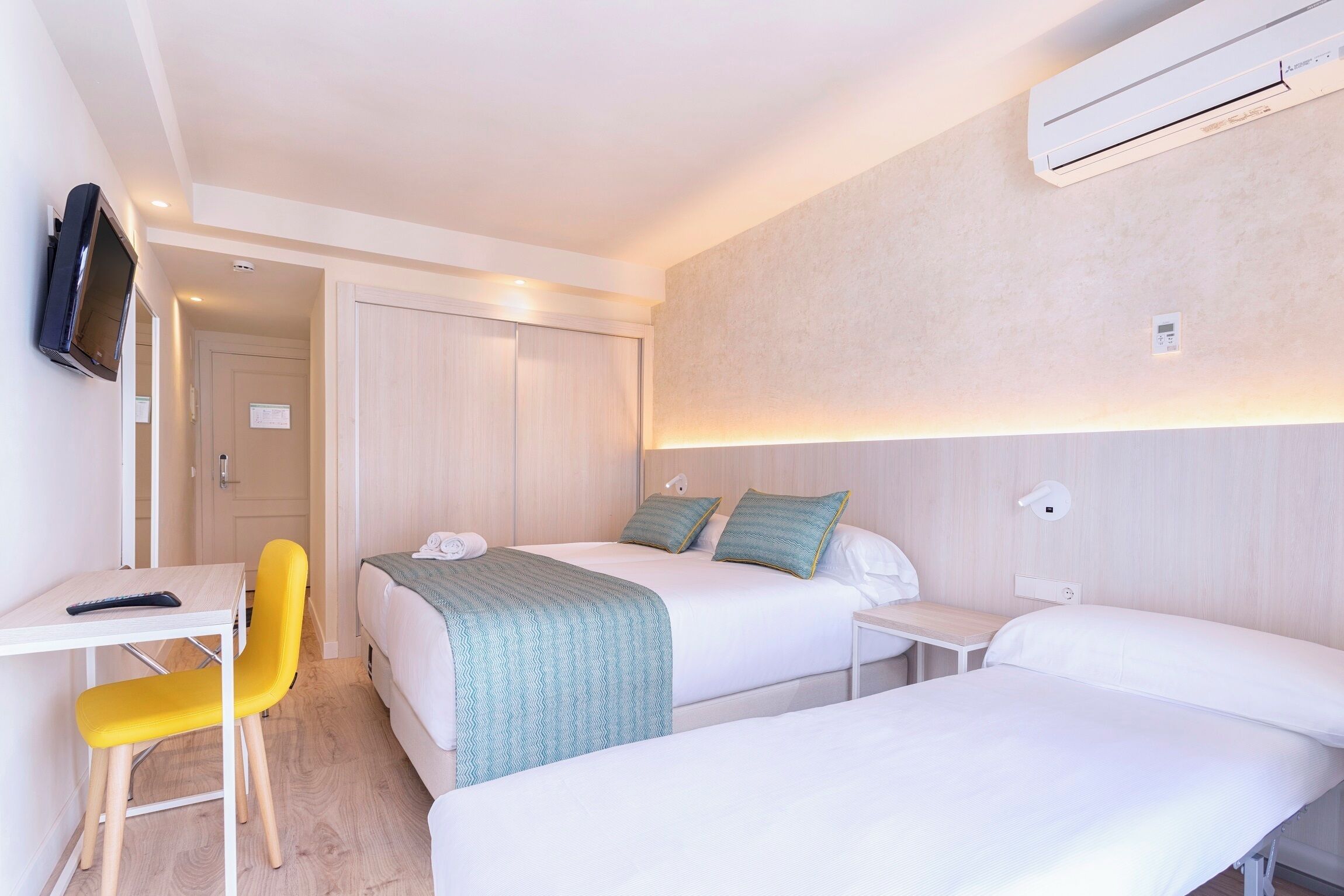 Een hotelkamer met twee bedden, een bureau, een stoel en een airconditioning.