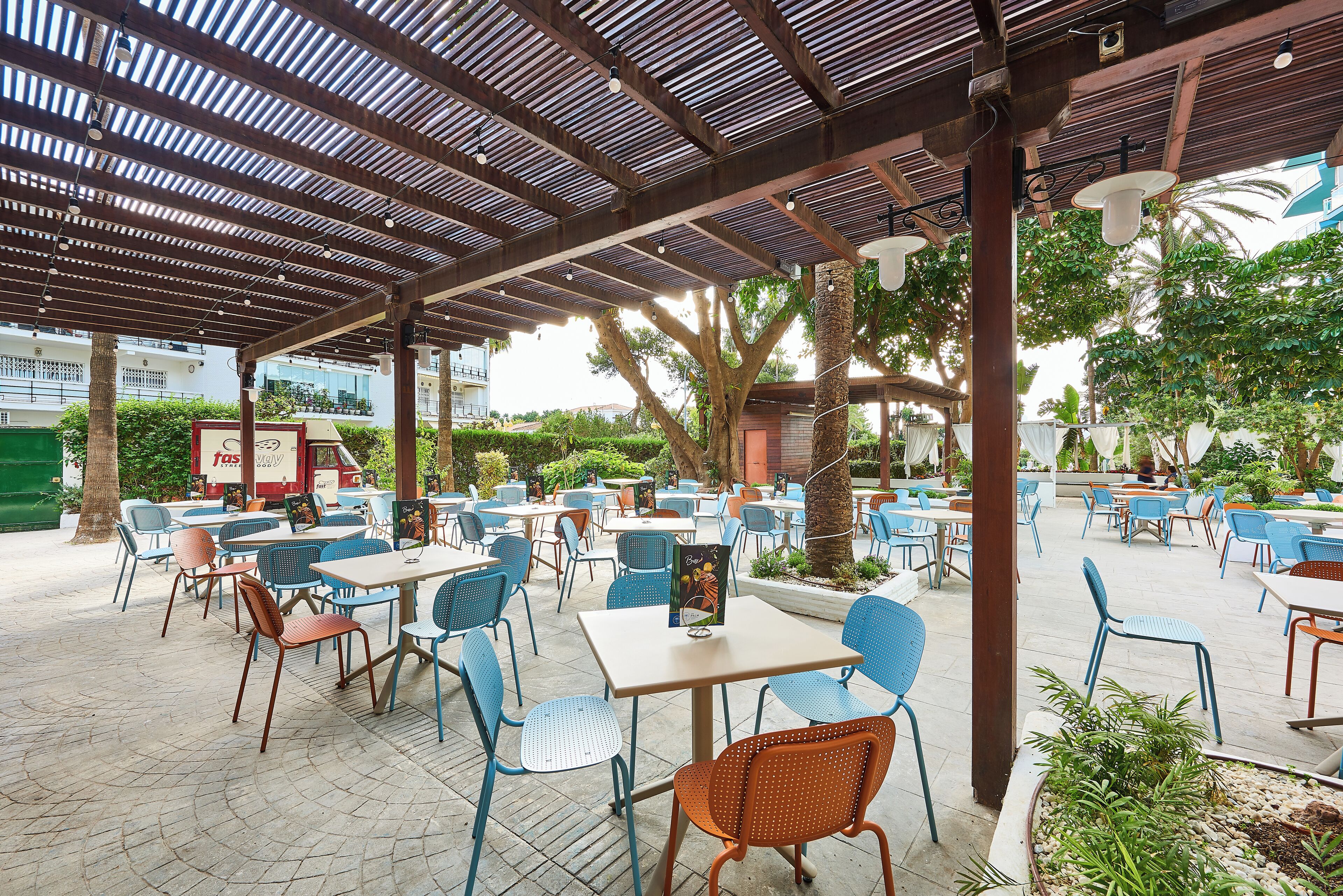 An outdoor cafe area with tables and chairs, a covered seating area, and a view of the surrounding buildings.