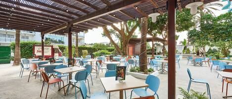 An outdoor cafe area with tables and chairs, a covered seating area, and a view of the surrounding buildings.