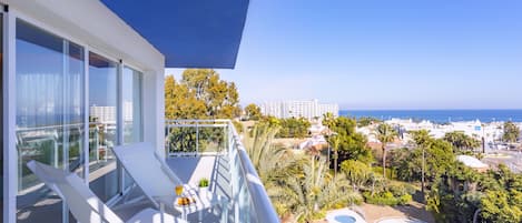Un balcon avec des chaises et une table blanches, d’où l’on a vue sur une piscine et sur le paysage urbain de la côte.