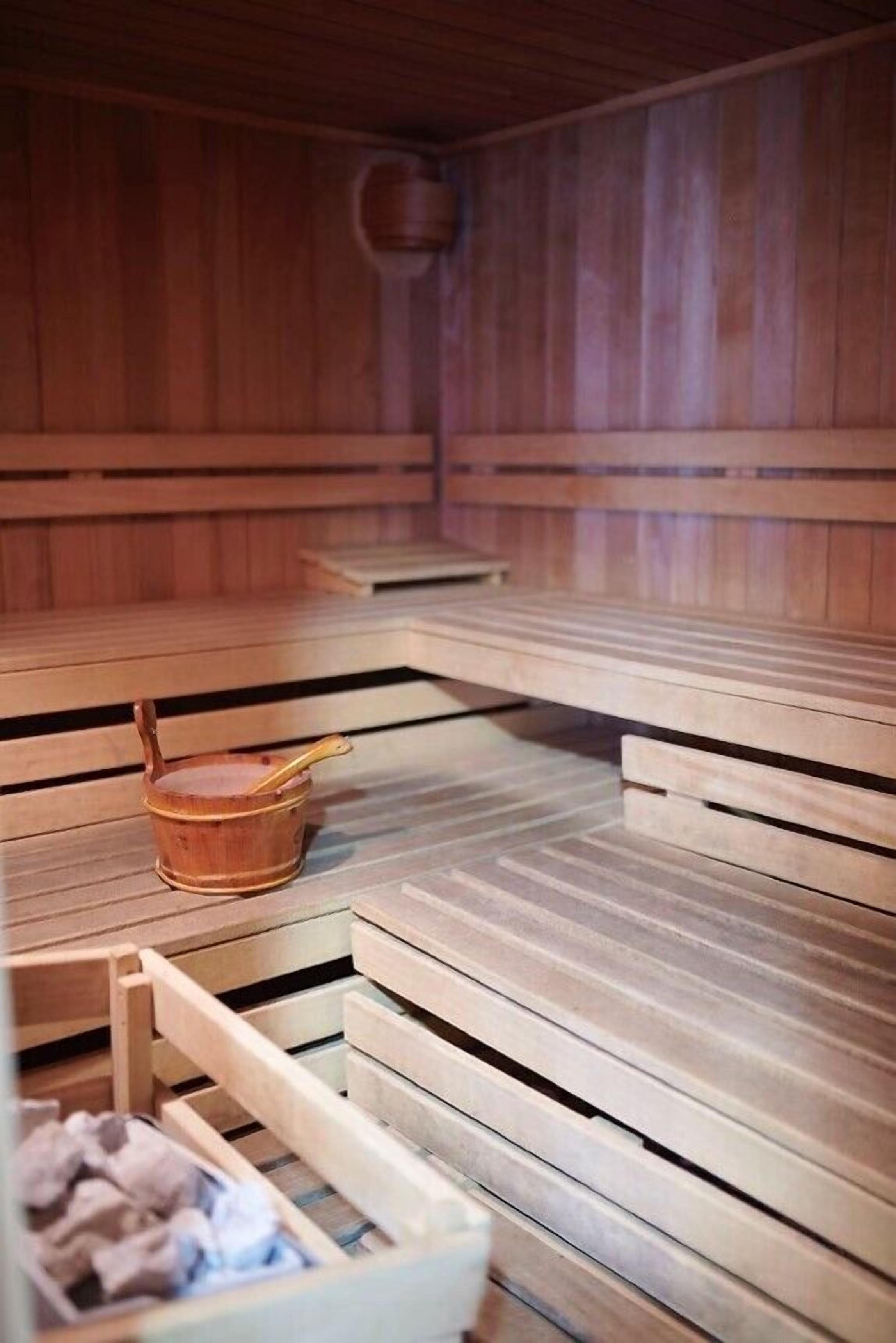 A wooden sauna with benches and a small wooden bucket.