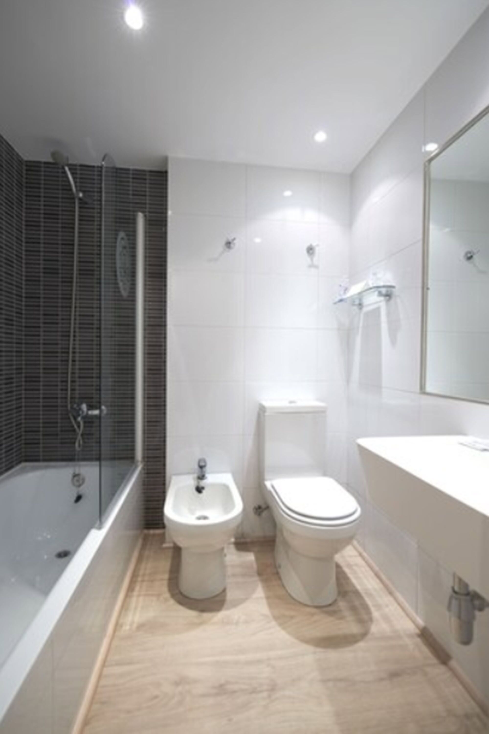 A modern bathroom with a bathtub, bidet, toilet, and a large mirror.