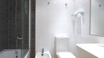A modern bathroom with a bathtub, bidet, toilet, and a large mirror.