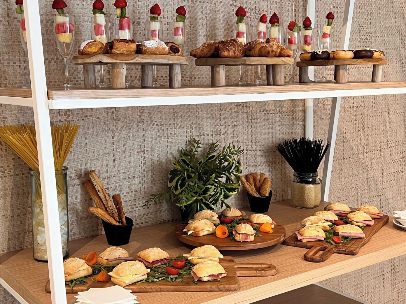 A buffet with various food items including pastries, sandwiches, and fruit skewers.