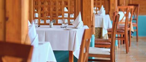 A row of wooden tables with white tablecloths, wooden chairs, and a patterned floor.
