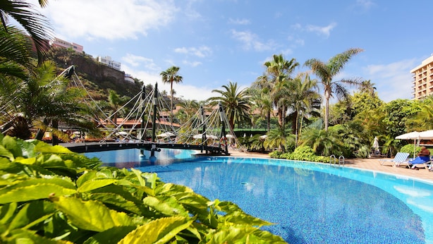 Una piscina con agua azul cristalina, rodeada de abundante vegetación y palmeras.