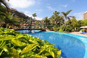 Una piscina con agua azul cristalina, rodeada de abundante vegetación y palmeras.