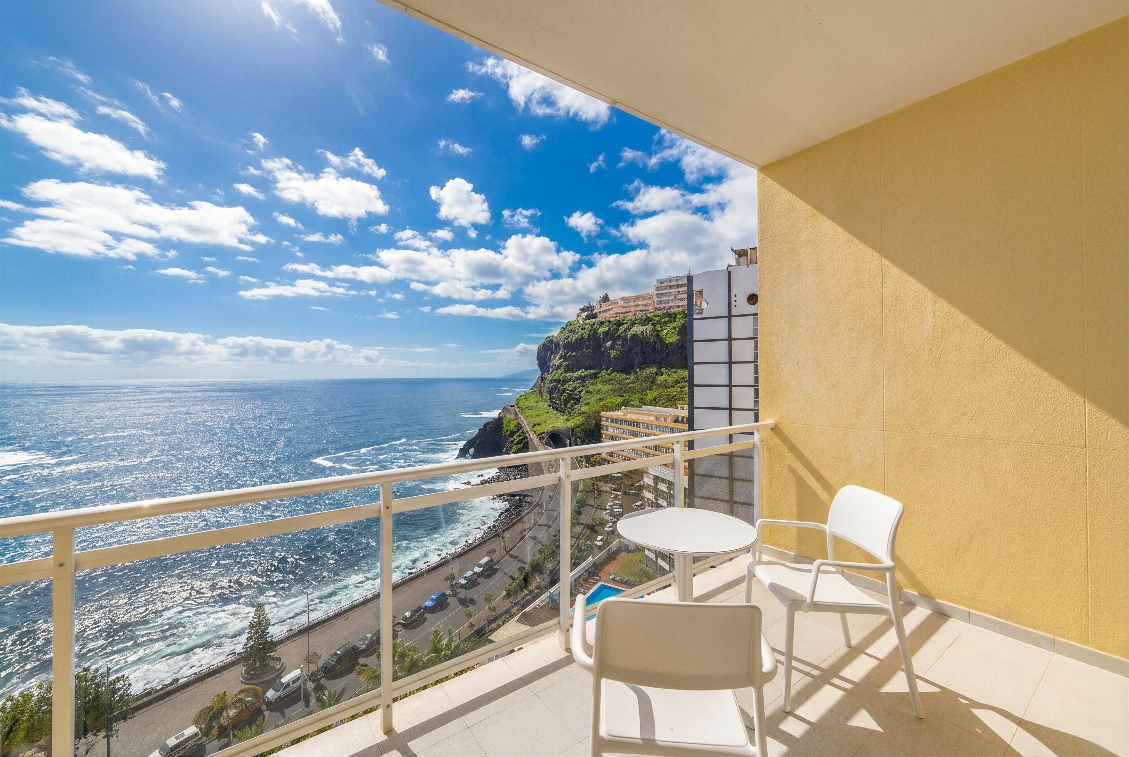 Un balcon avec vue sur l’océan, une route et un bâtiment situé au sommet d’une falaise.