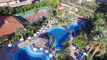 Un resort con varias piscinas, tumbonas y palmeras.
