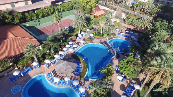 Un resort con varias piscinas, tumbonas y palmeras.