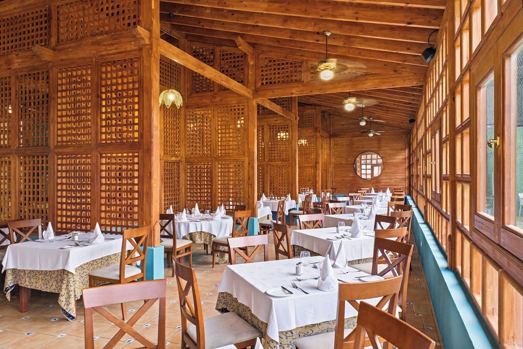 Un restaurant aux murs recouverts de treillis en bois, avec des tables rondes recouvertes de nappes blanches et des chaises en bois.