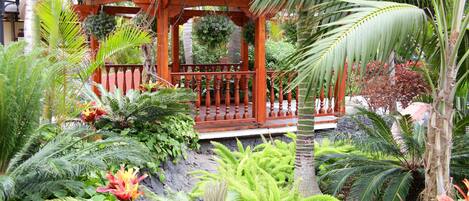Un belvédère en bois, entouré d’une végétation tropicale luxuriante, et un sentier pavé de pierres.