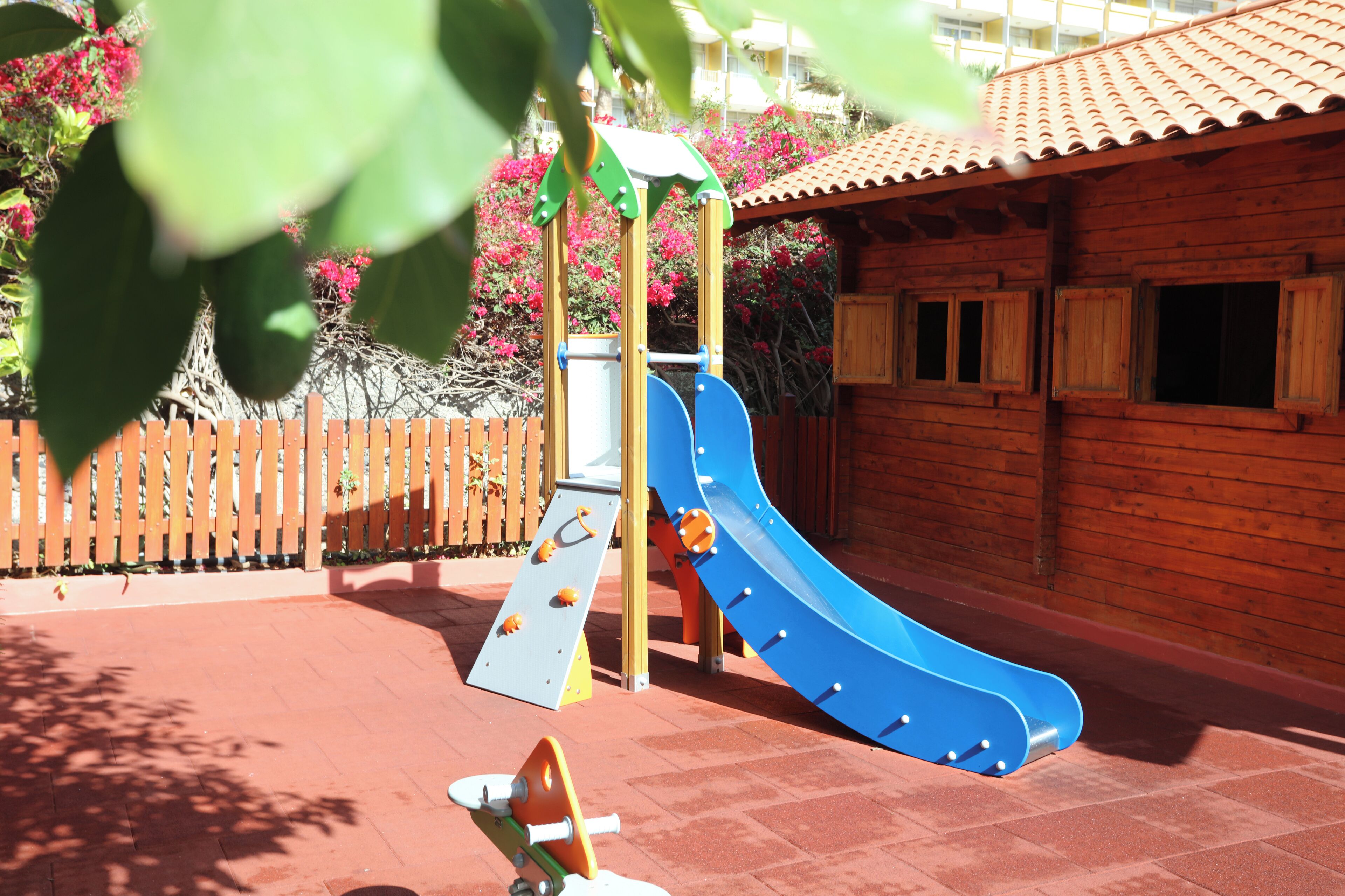 A playground with a blue slide, a climbing structure, and a wooden fence.