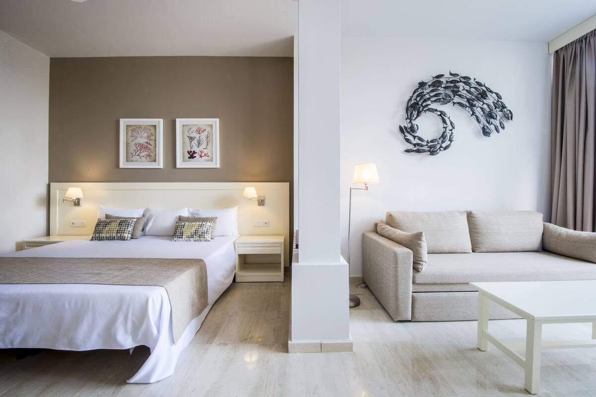 A hotel room with a bed, a sofa, a coffee table, and wall art.