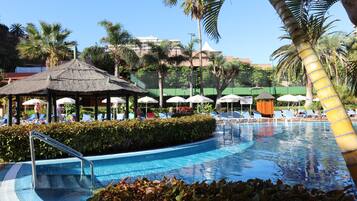 A swimming pool with lounge chairs and a thatched-roof gazebo.