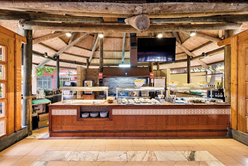 A rustic kitchen with a central island, wooden beams, and a tiled floor.