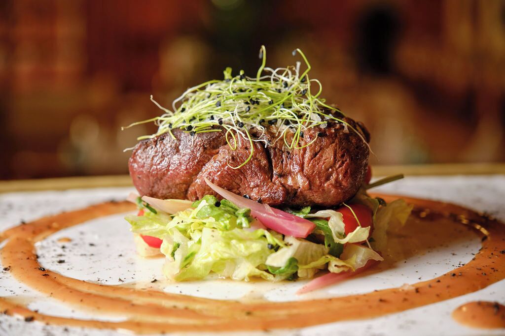 A steak topped with sprouts and a salad, served on a plate with sauce.