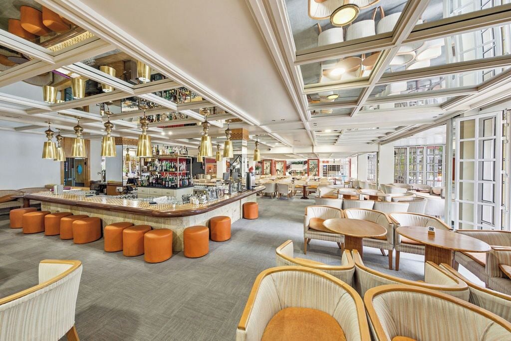 A spacious hotel lobby with a central bar area, multiple seating options, and large windows providing natural light.