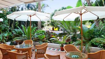 A patio area with wicker furniture, white umbrellas, and lush tropical plants.
