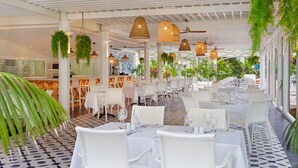 Un restaurante con mesas y sillas blancas, plantas colgantes y un ventilador de techo.