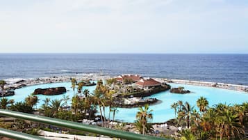 Un resort con una amplia piscina rodeada de palmeras y vistas al océano.