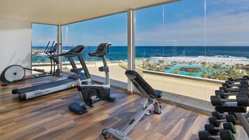 Un gimnasio con cintas de correr, una prensa de banca y mancuernas, con vistas a una playa y al océano.