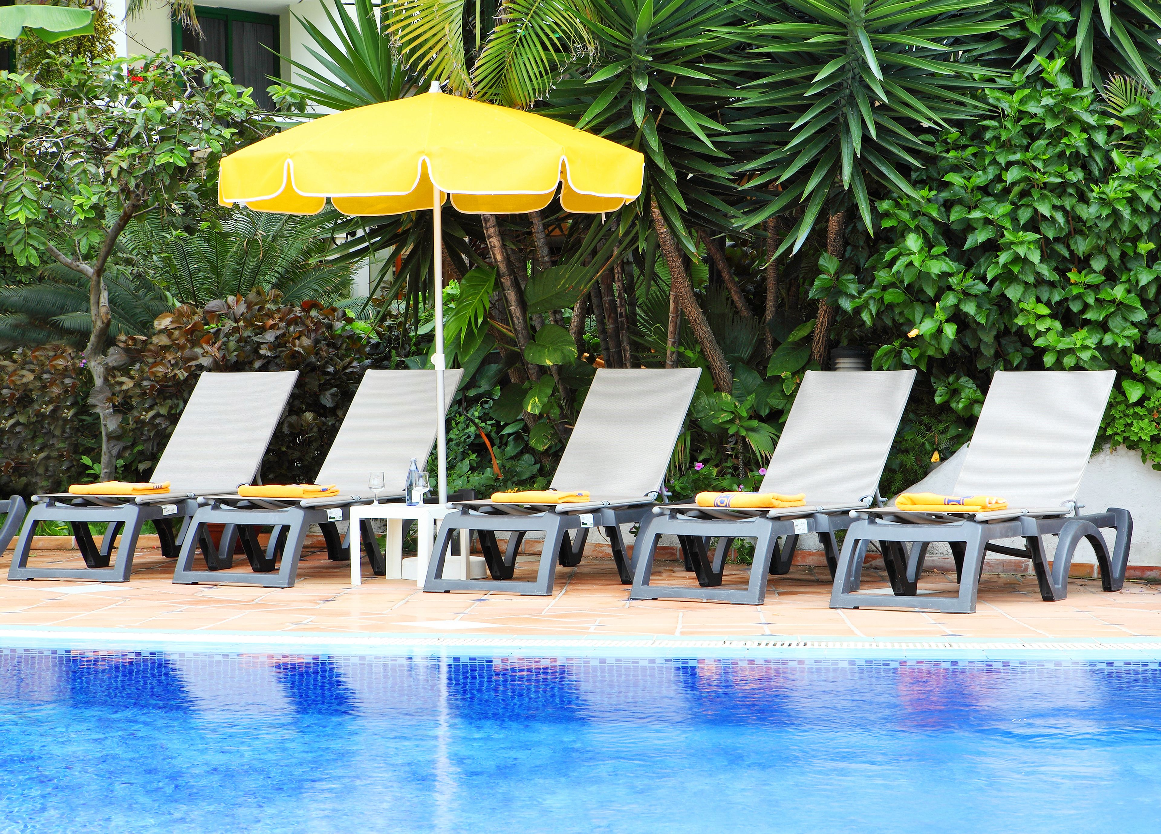 Uma área à beira da piscina com espreguiçadeiras e um guarda-sol amarelo.