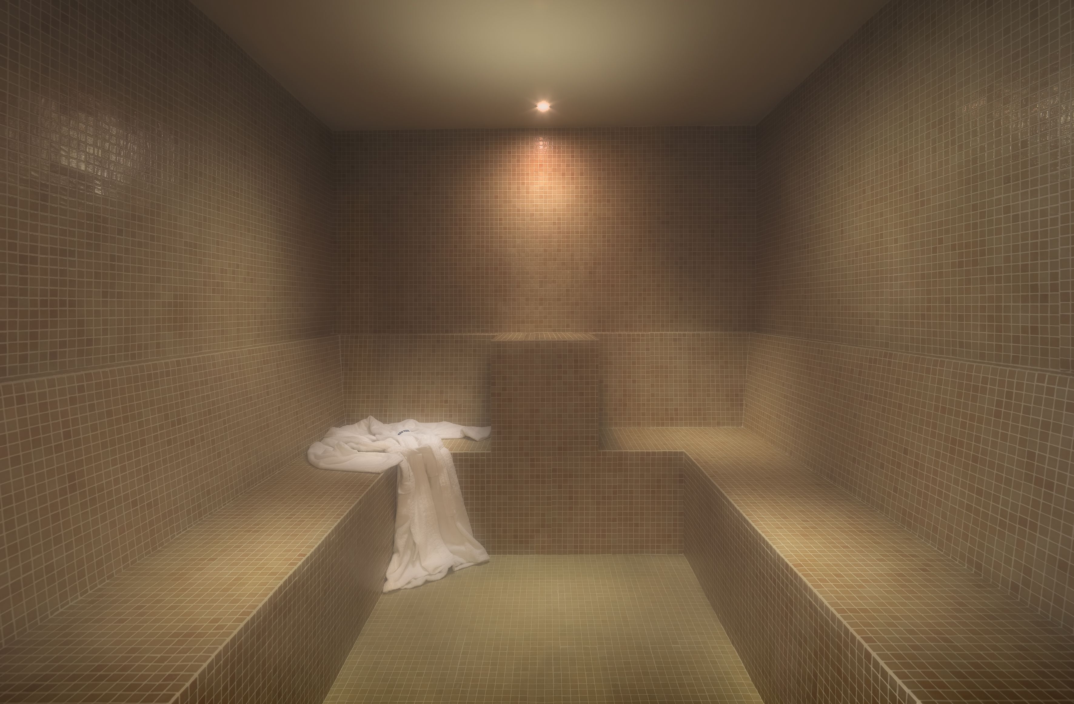 A tiled bathroom with a bench and a towel.
