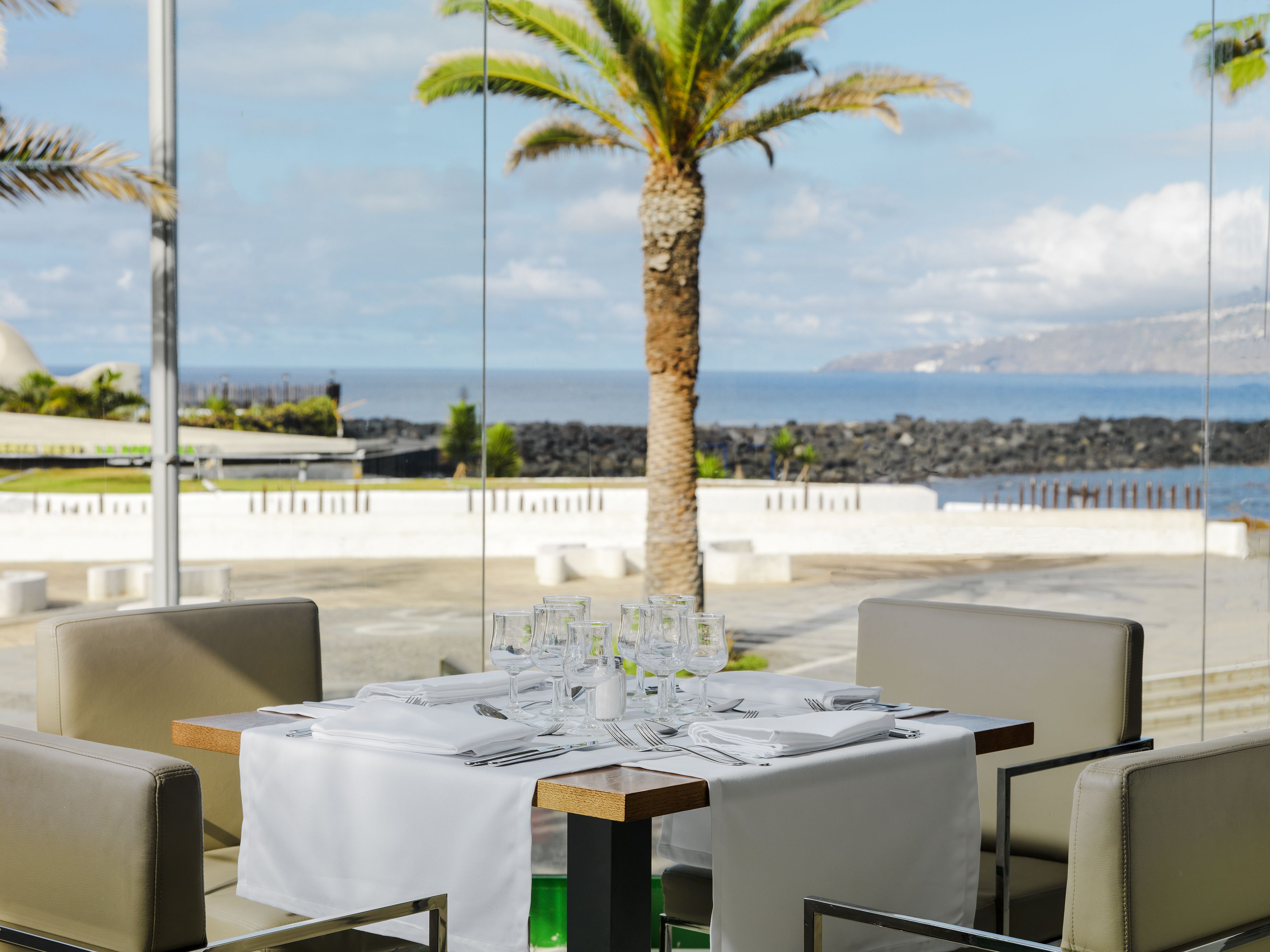 Uma mesa posta para refeição com vista para o oceano e uma palmeira.