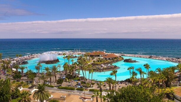 Un resort con piscina central, palmeras y vistas al océano.