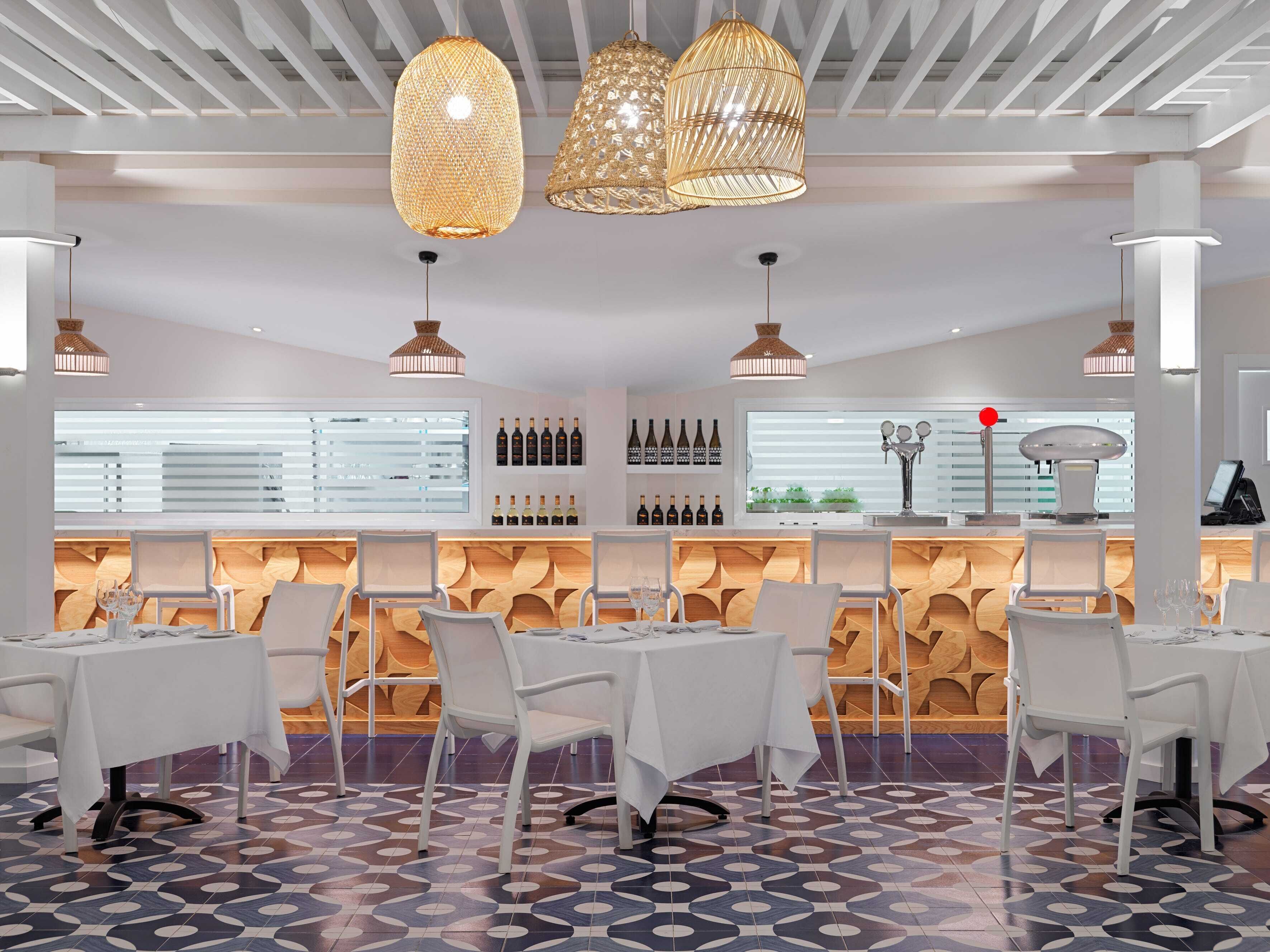 A modern restaurant interior with white tables, a patterned floor, and a wine display.