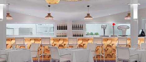 A modern restaurant interior with white tables, a patterned floor, and a wine display.