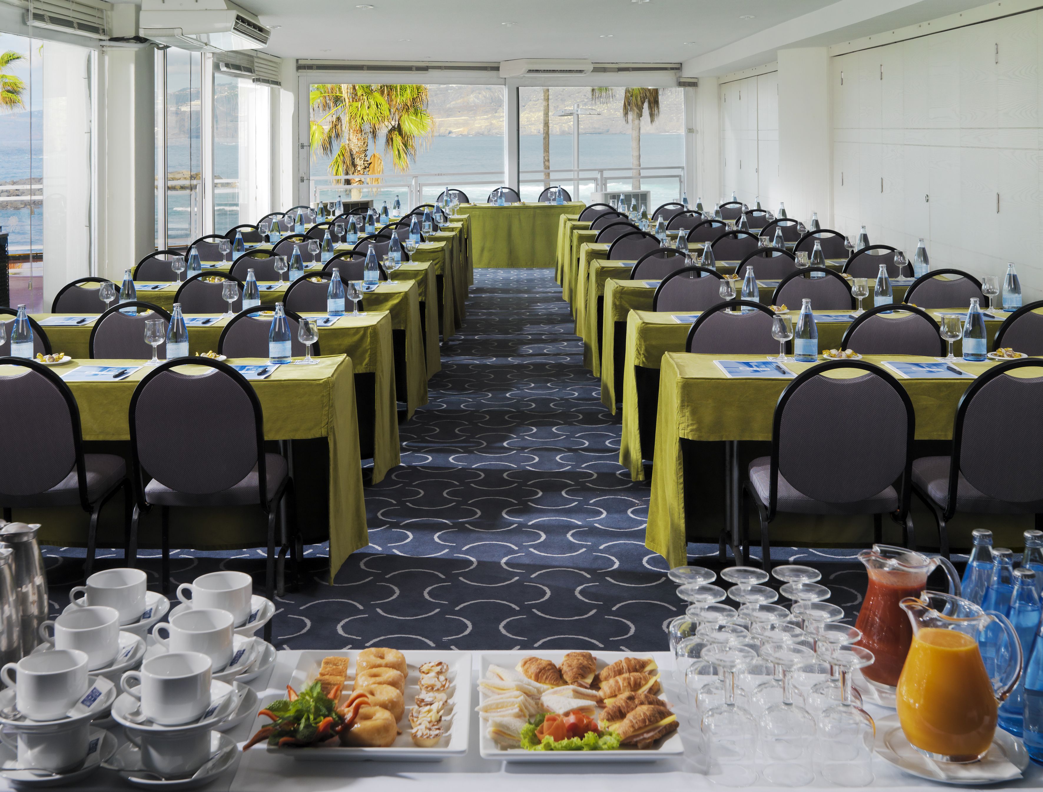 Ein Konferenzraum mit gedeckten Tischen für eine Besprechung, ausgestattet mit Wasserflaschen, Gläsern und einem Buffet mit Gebäck und Sandwiches.