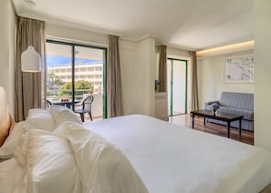 Habitación de hotel con una cama grande, una mesita con un florero, un sofá y vistas al balcón exterior.