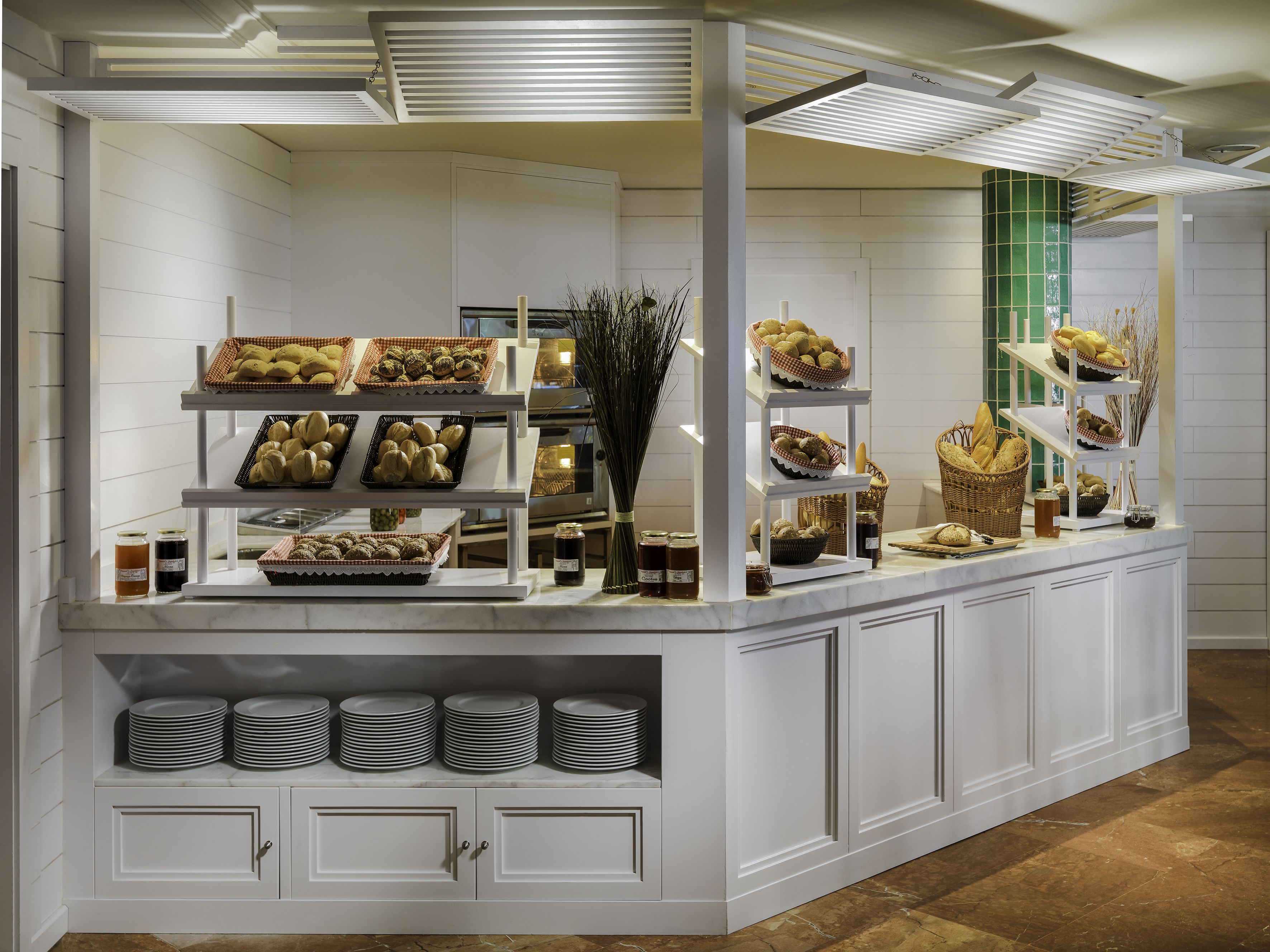 Una mesa de buffet con diferentes alimentos expuestos en estantes y bandejas, incluyendo panes, pasteles y frascos con salsas.