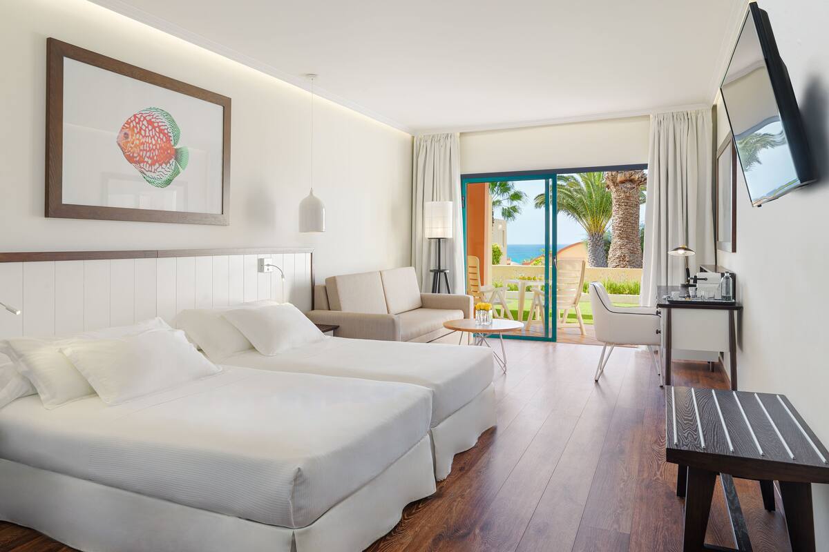 Une chambre d’hôtel avec deux lits, un bureau, une chaise, une télévision et un balcon donnant sur la mer.