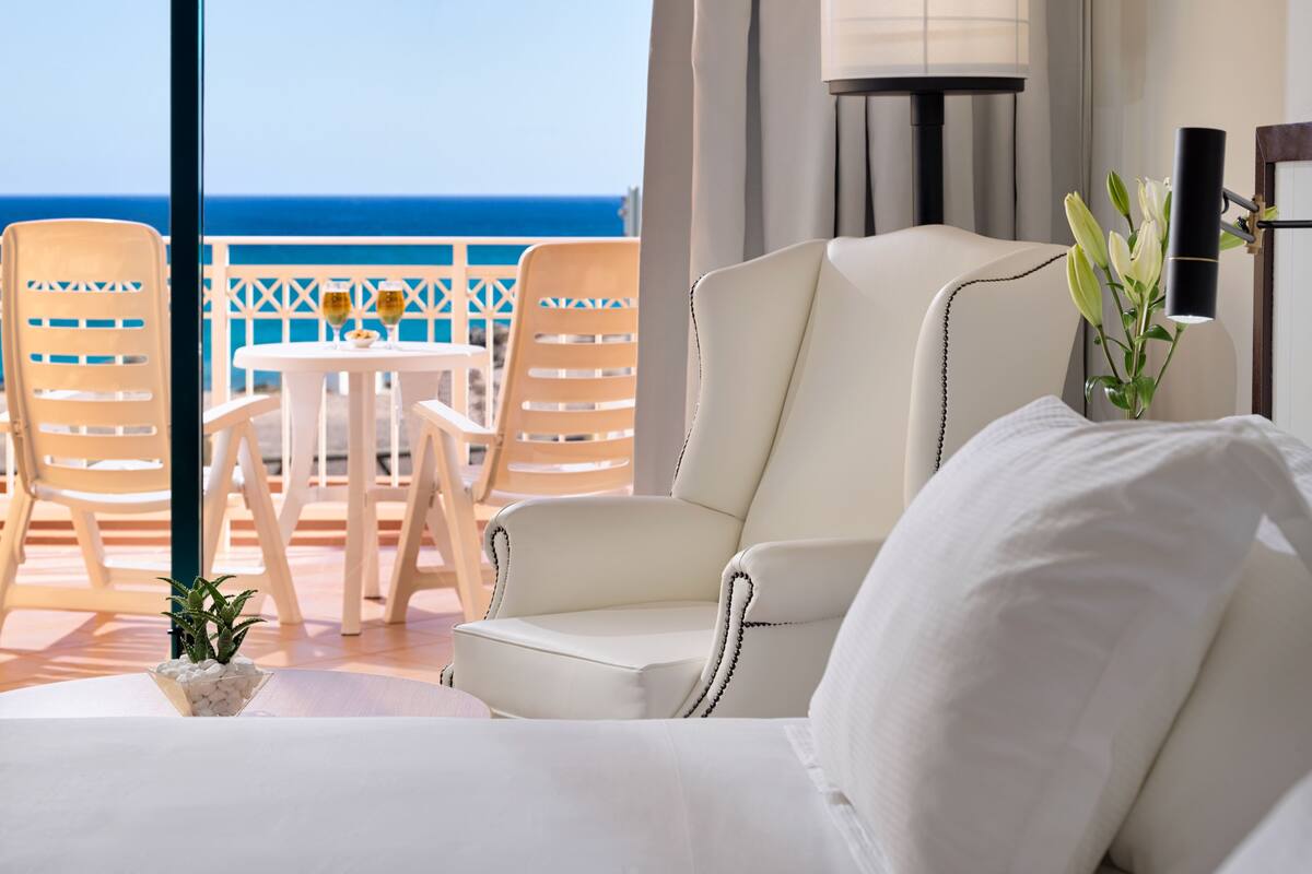 Une chambre d’hôtel avec un balcon, des meubles blancs, une petite table avec des boissons et une vue sur la mer.