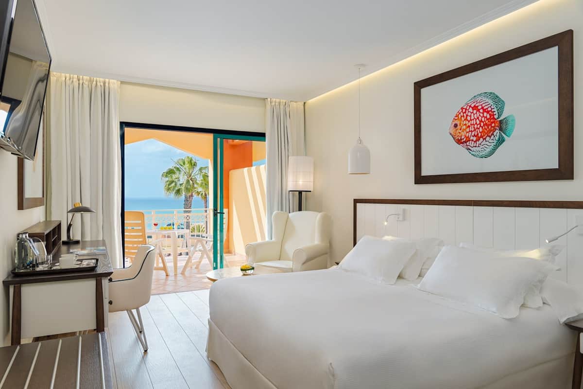 Une chambre d’hôtel équipée d’un lit, d’un bureau, d’une chaise, d’une télévision et d’un balcon avec vue sur la mer.