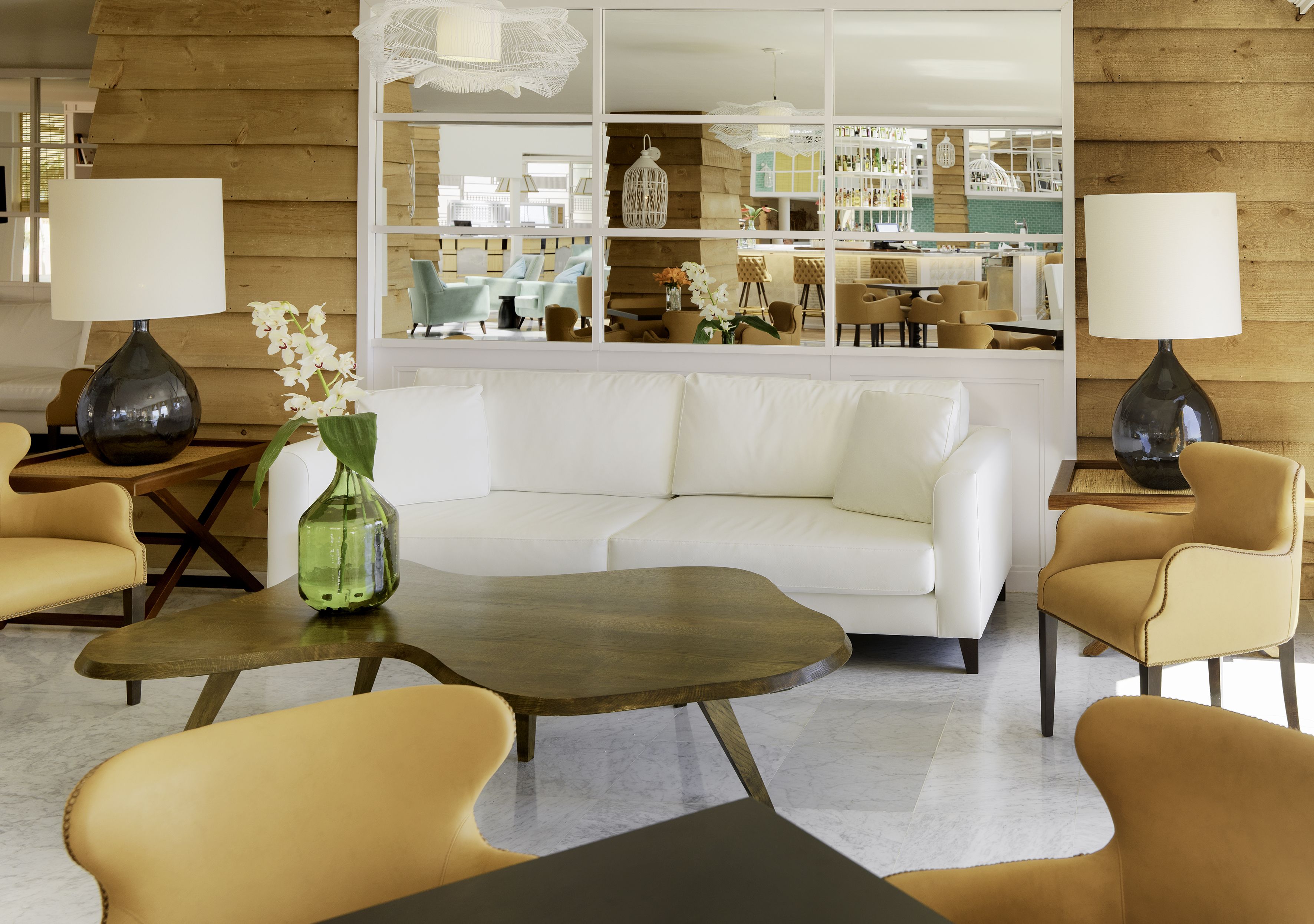 A modern living room with a white sofa, two armchairs, a coffee table, and a large mirror reflecting the room.