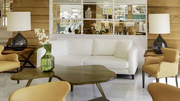 A modern living room with a white sofa, two armchairs, a coffee table, and a large mirror reflecting the room.
