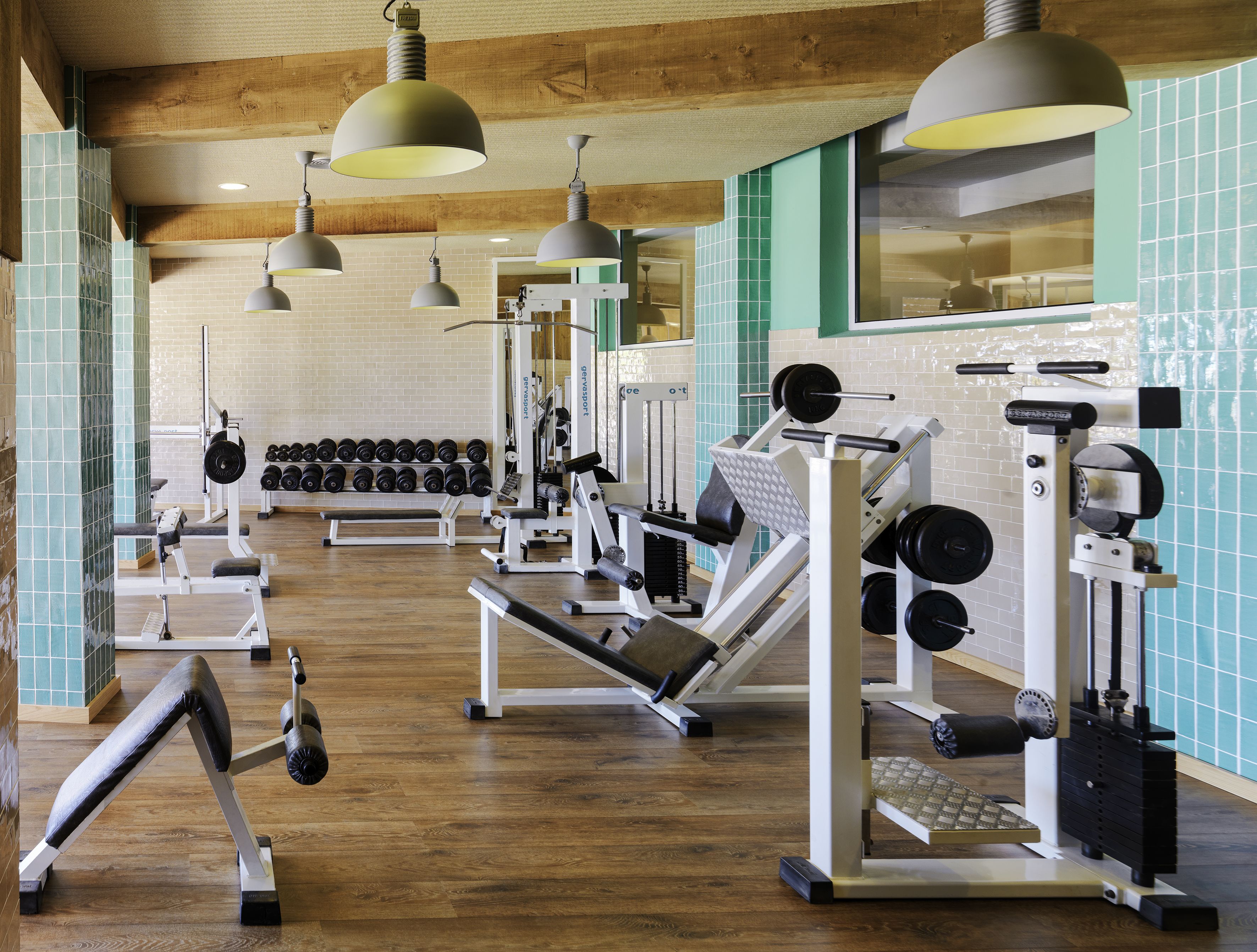 Un gimnasio con diferentes equipos de ejercicio, pisos de madera y paredes de azulejos verdes.