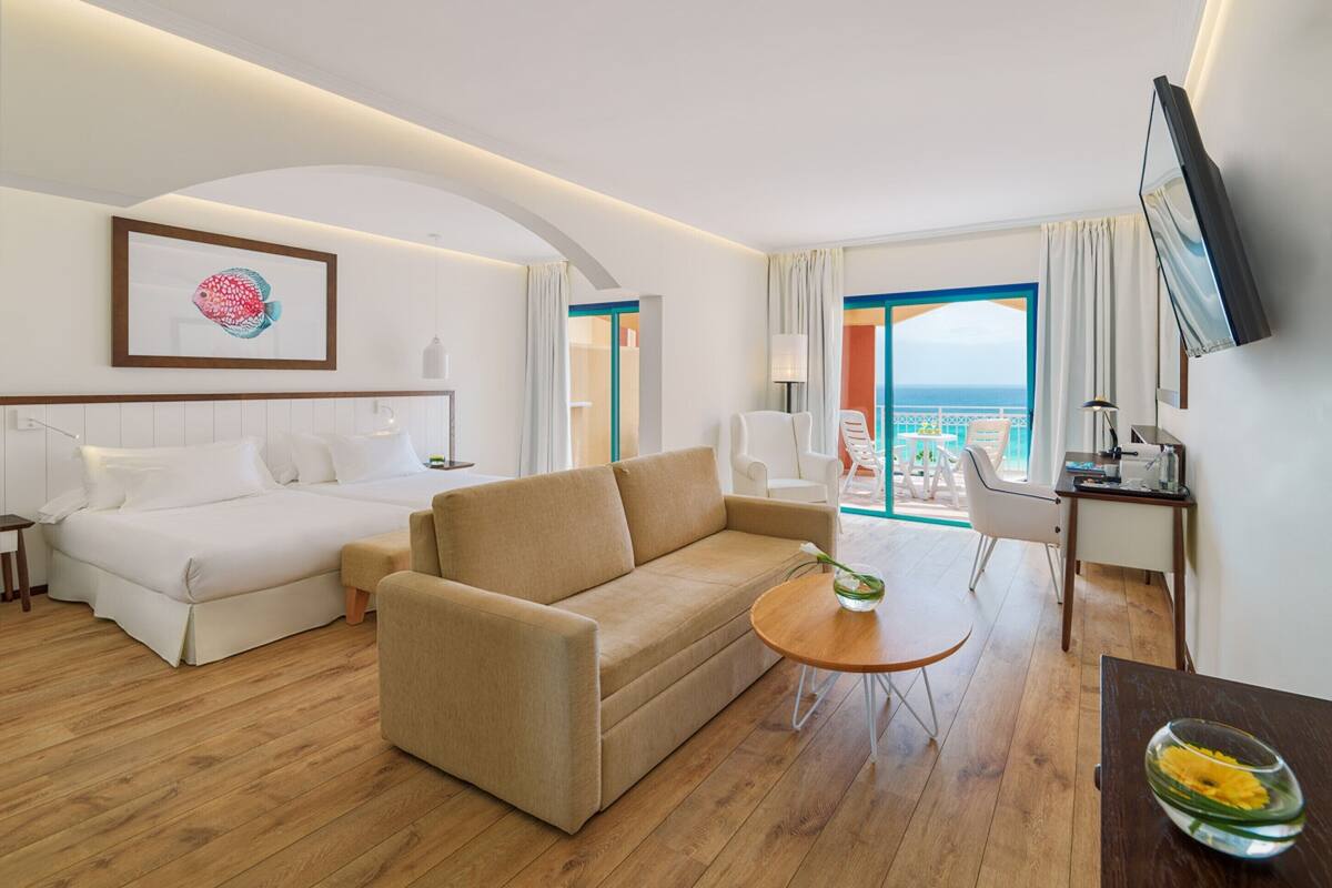 Une chambre d’hôtel comprenant un lit, un canapé, une petite table, une télévision et un balcon avec vue sur la mer.