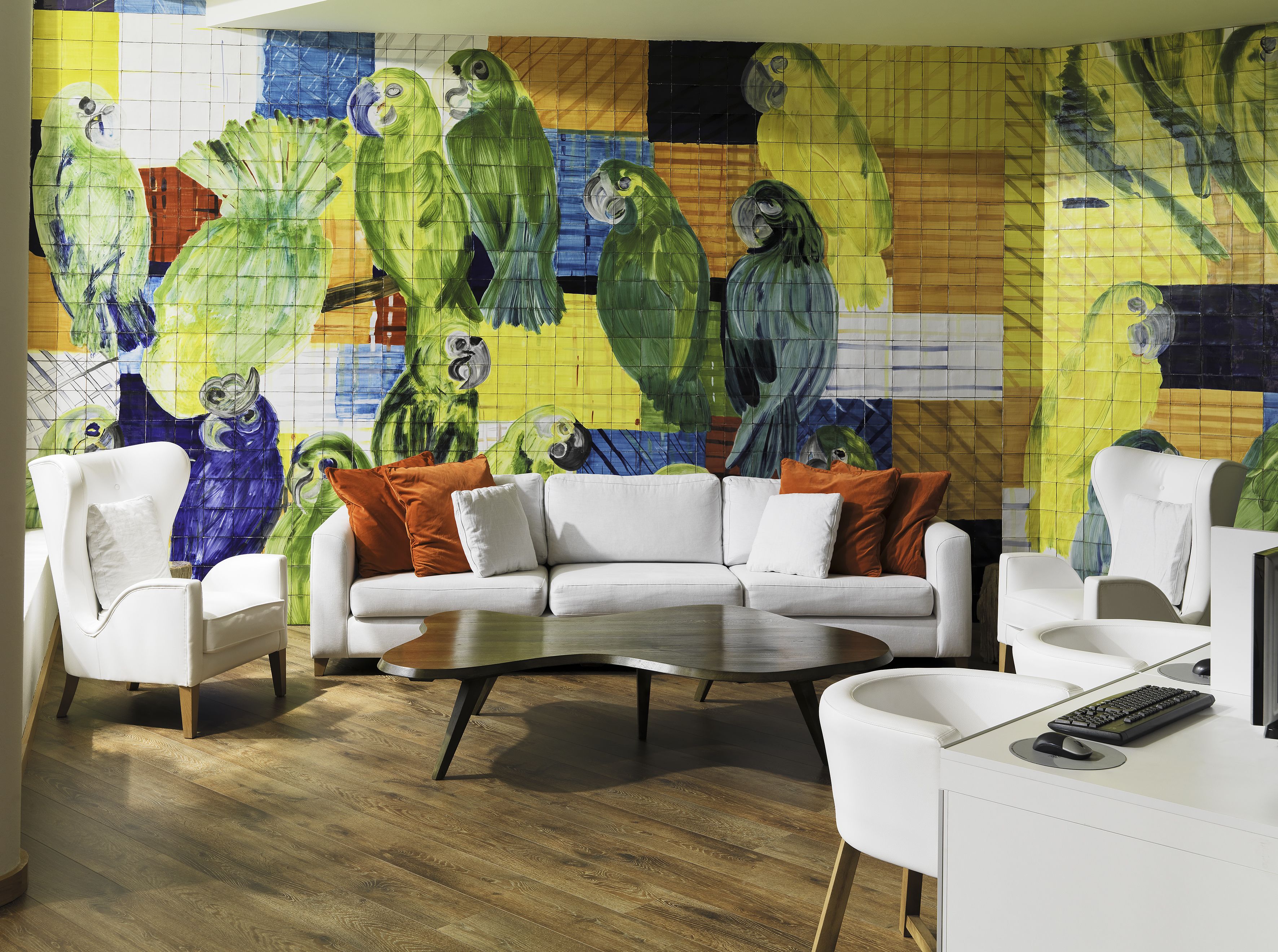 Una sala de estar moderna con un sofá blanco, dos sillones, una mesa de centro y un mural grande y colorido de loros en la pared.