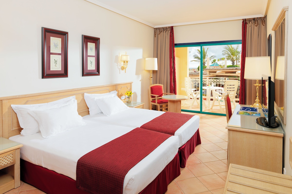A hotel room with a large bed, a desk with a computer, and a balcony with outdoor seating.