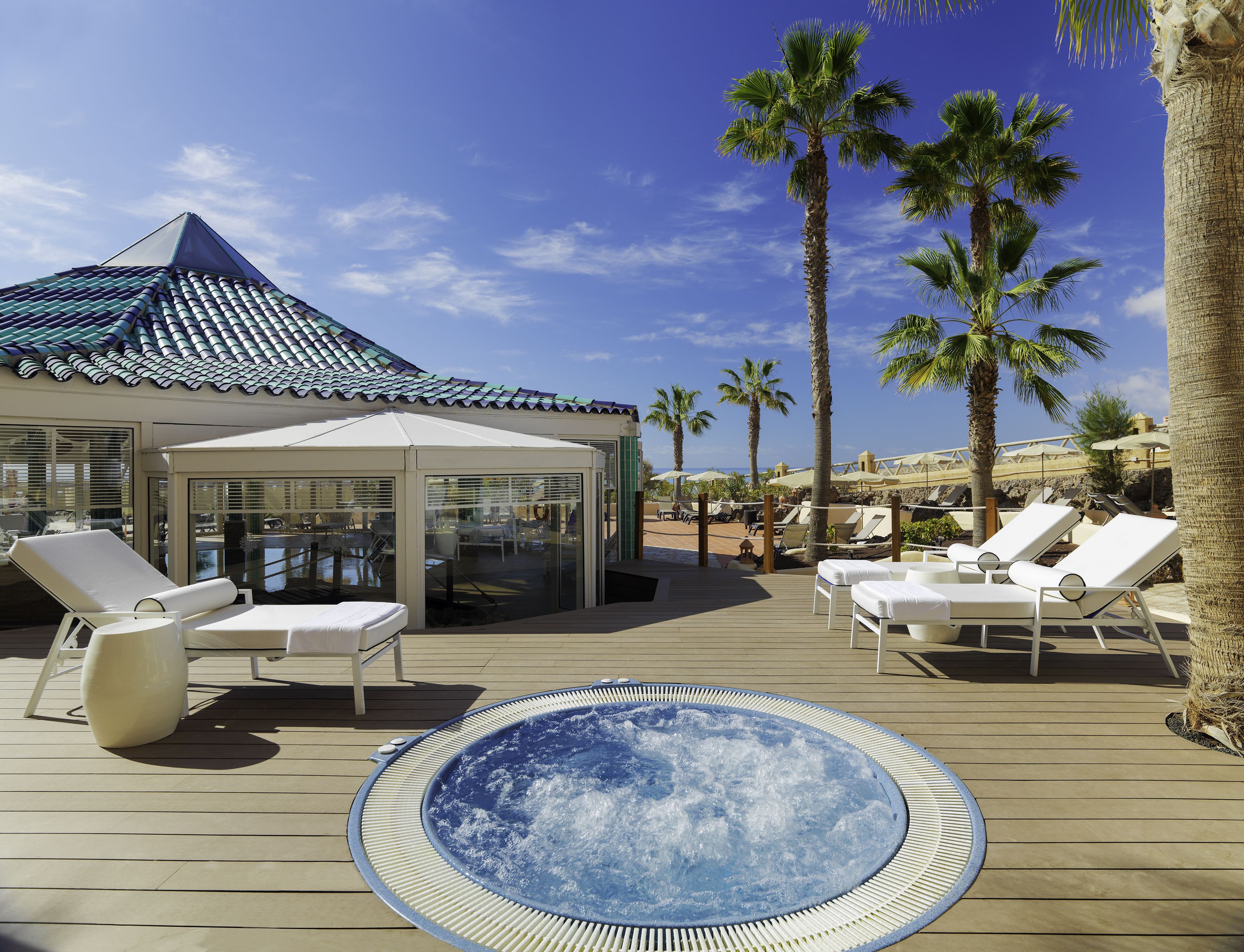 Un área junto a la piscina con sillones de descanso, un jacuzzi y palmeras.